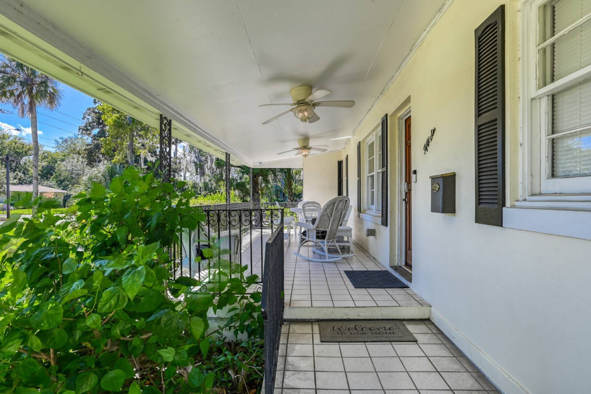 A covered porch with a ceiling fan, outdoor seating, and a welcome mat.