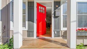 Una entrada de casa con puerta roja, un porche cubierto y vista al interior.
