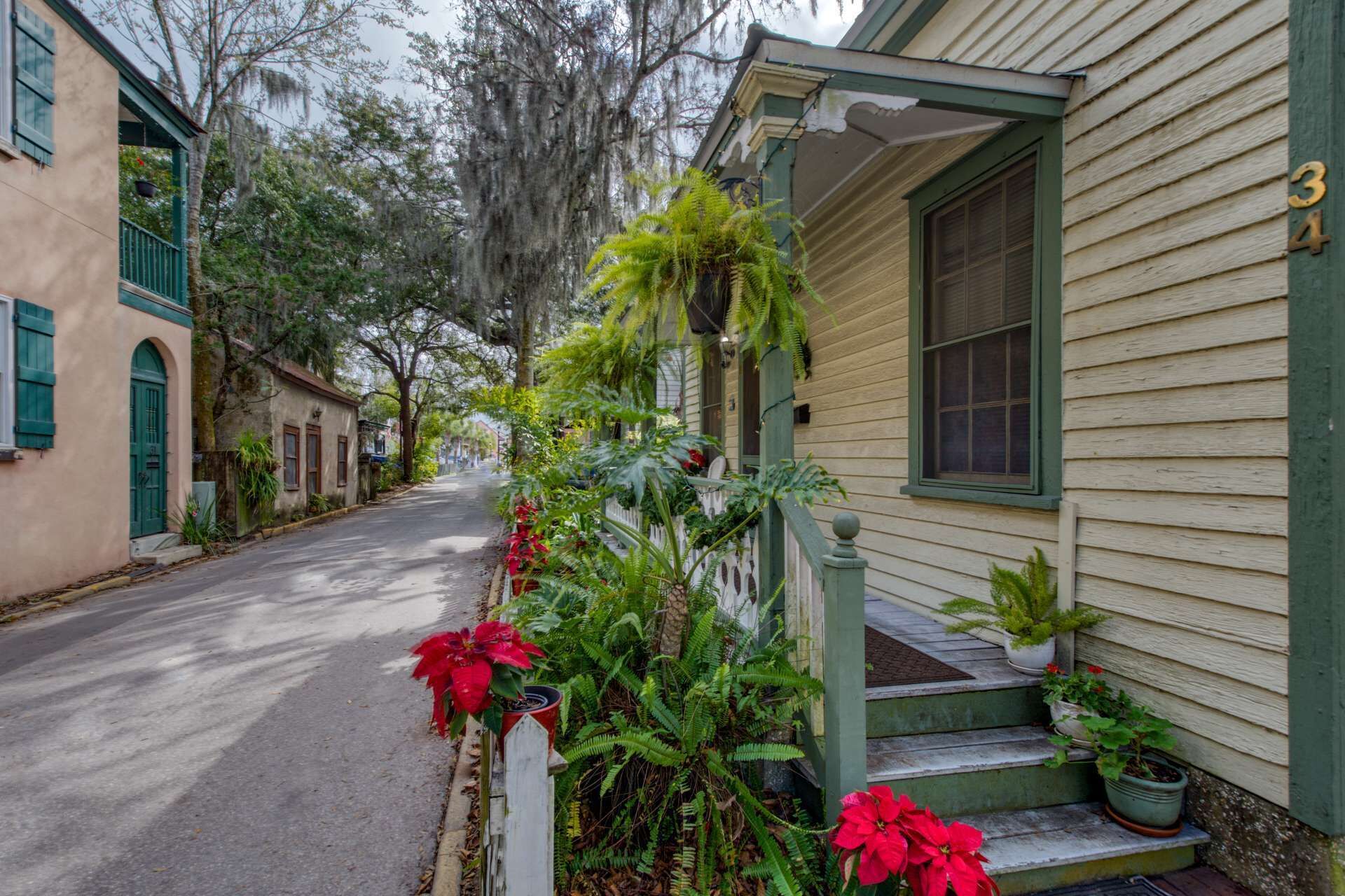 Una calle estrecha bordeada de casas históricas, cada una con un porche y plantas en macetas.