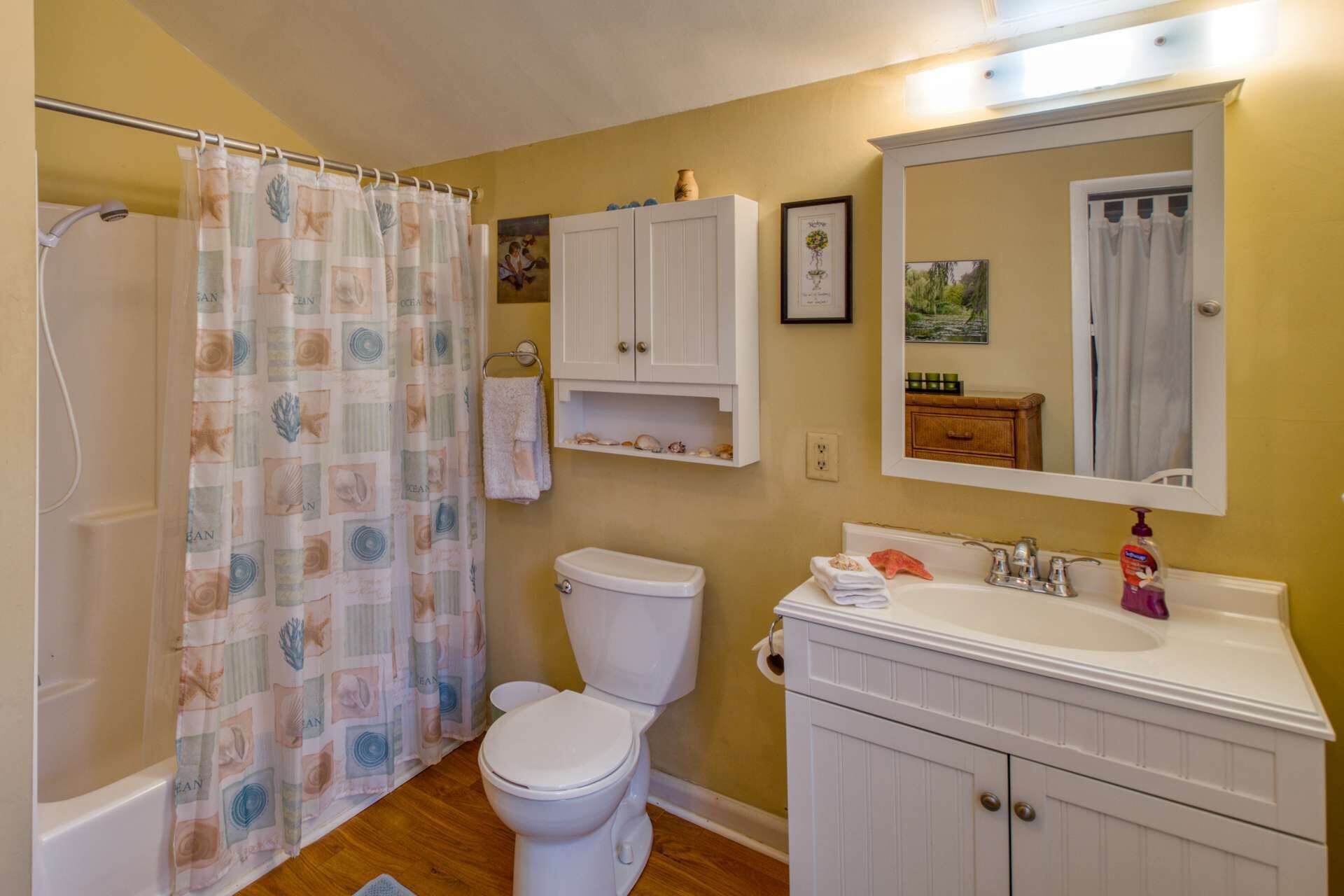 A bathroom with a shower curtain, toilet, sink, and cabinets.