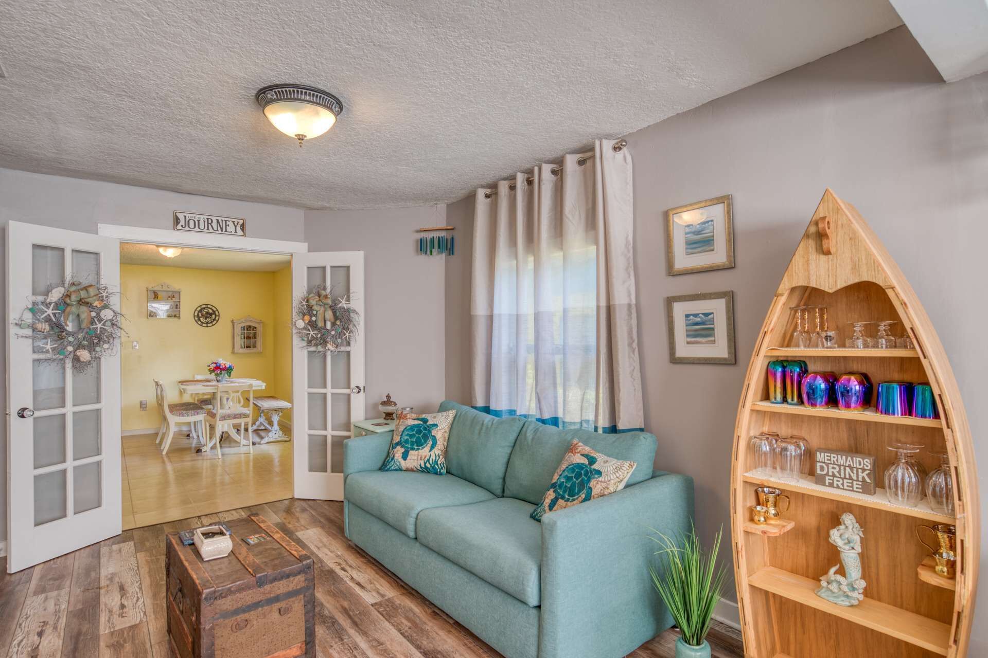 Ein Wohnzimmer mit einem türkisfarbenen Sofa, einem hölzernen Bücherregal und einer Tür mit der Aufschrift "JOURNEY".