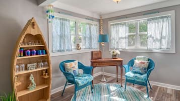 Ein Zimmer mit einem hölzernen Bücherregal, zwei blauen Sesseln, einem runden Teppich und einem Schreibtisch mit Lampe.