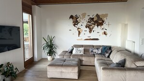 En opholdsstue med en stor modulsofa, et fladskærms-tv og et verdenskort på væggen.