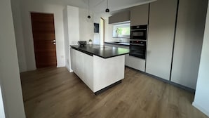Et moderne køkken med en central ø, indbygget ovn og hængende lamper.