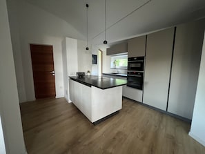 Moderni keittiö, jossa on keskeinen saareke, sisäänrakennettu uuni ja riippuvalaisimet.