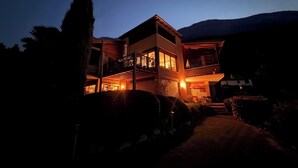 Un edificio moderno de dos pisos con balcones y ventanas amplias, rodeado de un paisaje montañoso.