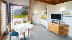 Un comedor con mesa y sillas, una cocina con televisor y vistas a las montañas desde la ventana.