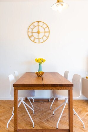 Une table de salle à manger en bois, sur laquelle est posé un vase rempli de fleurs jaunes, entourée de chaises blanches.
