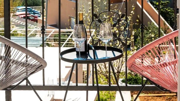 Un balcón con mesa y sillas, con vistas a un paisaje costero con edificios y árboles.