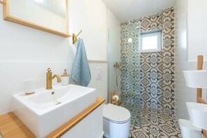 Une salle de bain avec un lavabo blanc, un robinet doré et des toilettes. Une serviette bleue est suspendue à un porte-serviettes. Les murs sont recouverts de carreaux décorés.