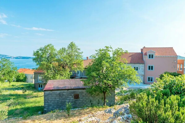 Une propriété située sur la côte, comprenant une maison en pierre, un bâtiment plus grand de couleur rose et une vue sur la mer.