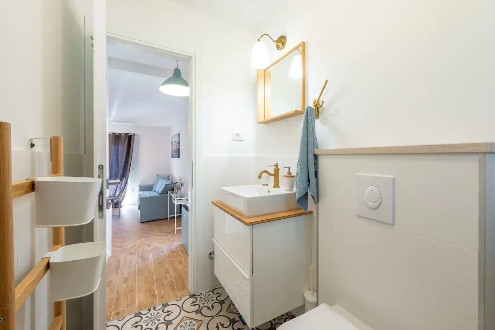 Uma casa de banho moderna com lavatório, espelho e porta-toalhas. Uma porta dá acesso a uma zona de estar com sofá e mesa.