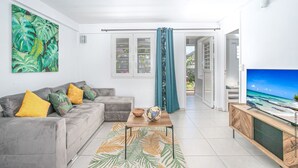 A modern living room with a grey sofa, a coffee table, and a television on a wooden cabinet. - Villa Ajoupa (SAINTE ANNE)