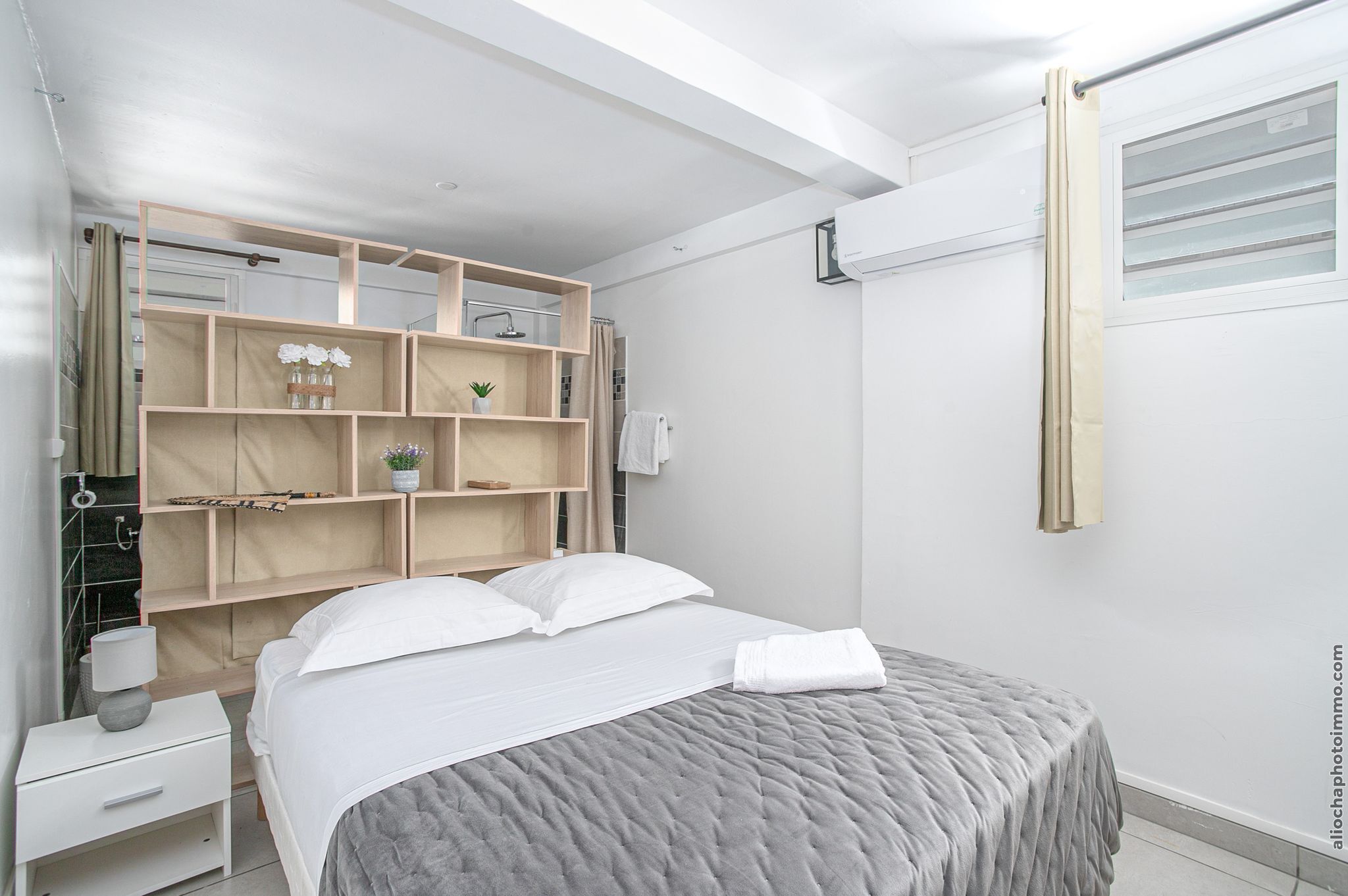 A modern bedroom with a bed, a nightstand, a built-in shelving unit, and a window with curtains.