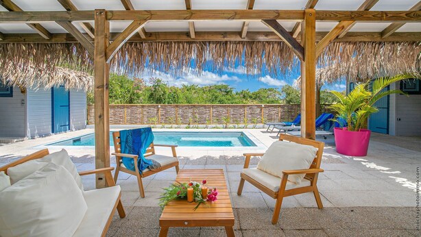 A covered outdoor area with a pool, wooden furniture, and a view of greenery. - Villa Ajoupa (SAINTE ANNE)