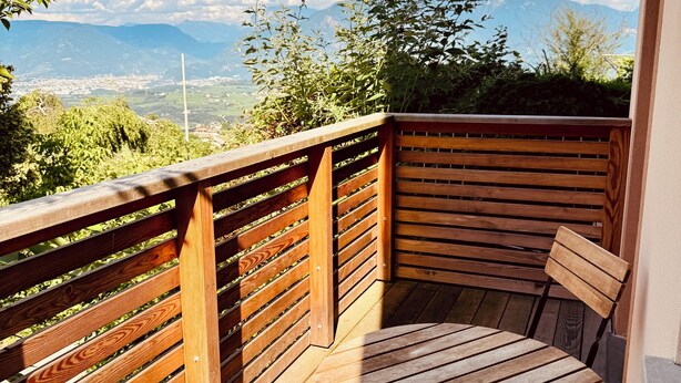Una terraza de madera con una mesa y sillas, con vistas a un paisaje montañoso.