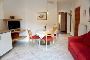 A dining area with a table, chairs, a television, and a red sofa.