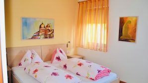 Una cama doble con ropa de cama floral, una mesita de noche, una lámpara de pared y dos cuadros.