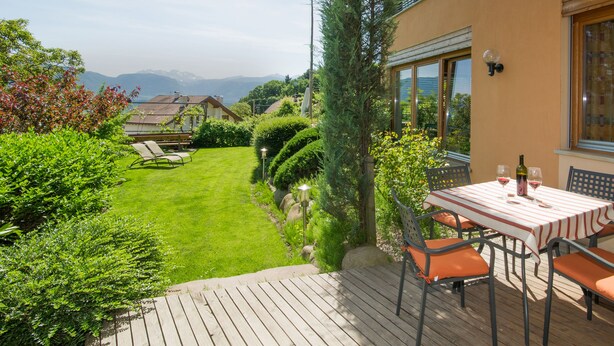 Une terrasse avec une table et des chaises, une vue sur une montagne et un jardin bien entretenu.