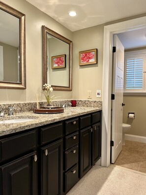 A bathroom with dark cabinetry, a granite countertop, a large mirror, and a door leading to another room. - “The Cradle Cottage", 3 bed-2 bath, renovated condo a short walk to Pinehurst CC (Pinehurst)