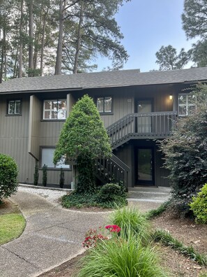 A two-story building with a balcony, a staircase, and a well-maintained garden with gravel paths and various plants. - “The Cradle Cottage", 3 bed-2 bath, renovated condo a short walk to Pinehurst CC (Pinehurst)
