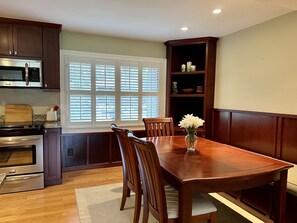 A kitchen with wooden cabinets, a dining table with chairs, a microwave, an oven, and a window with blinds. - “The Cradle Cottage", 3 bed-2 bath, renovated condo a short walk to Pinehurst CC (Pinehurst)