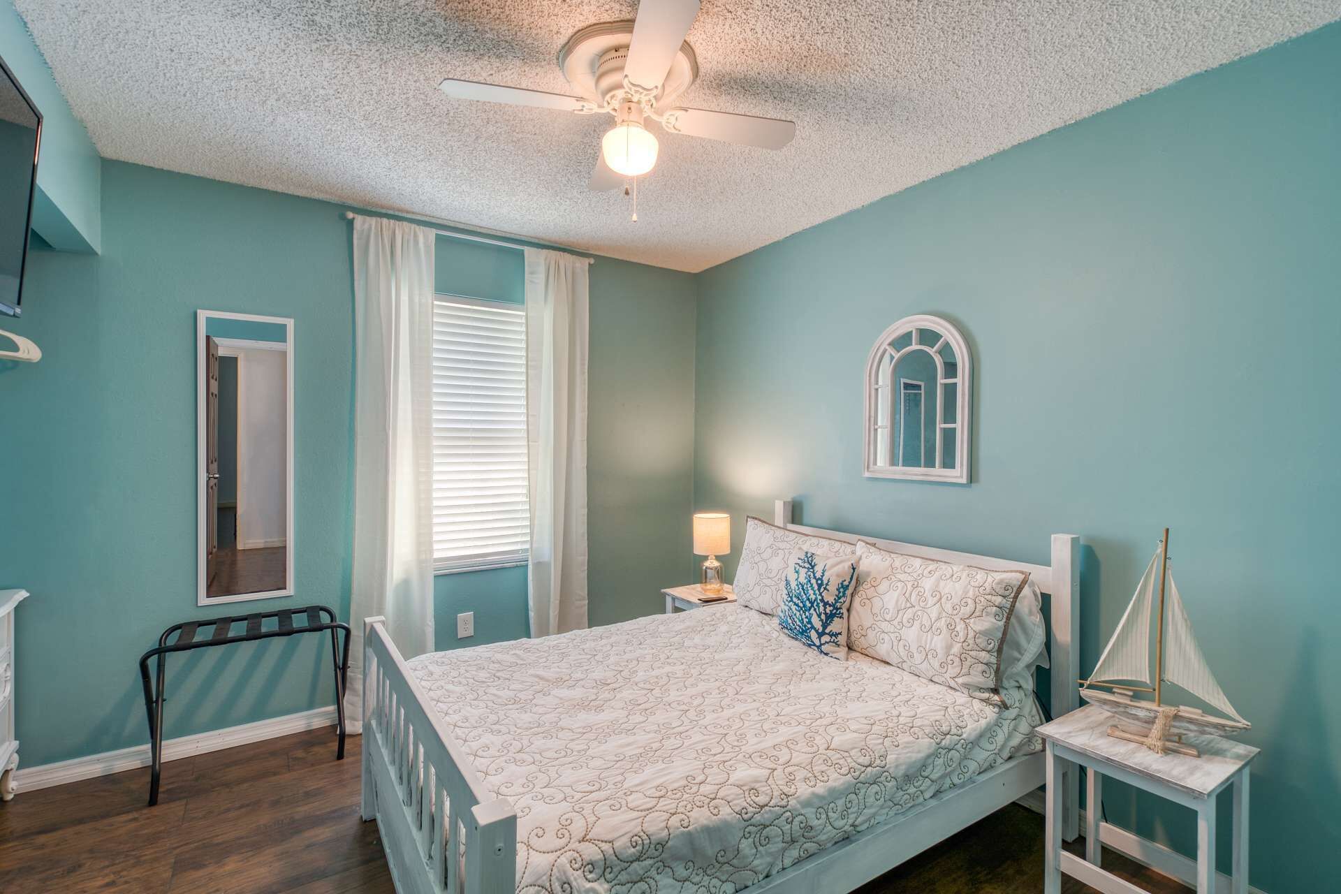 A bedroom with a bed, a nightstand, a ceiling fan, a window with blinds, and a small sailboat model.