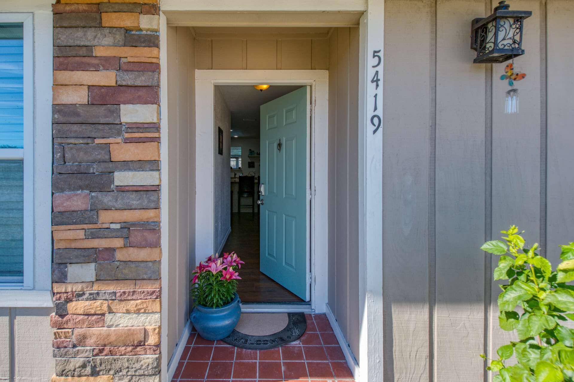 A house entrance with a stone wall, a blue door, and a number '5419' on the wall.