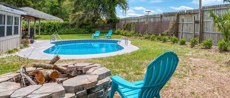 Un giardino sul retro con piscina, un braciere e due sedie blu.