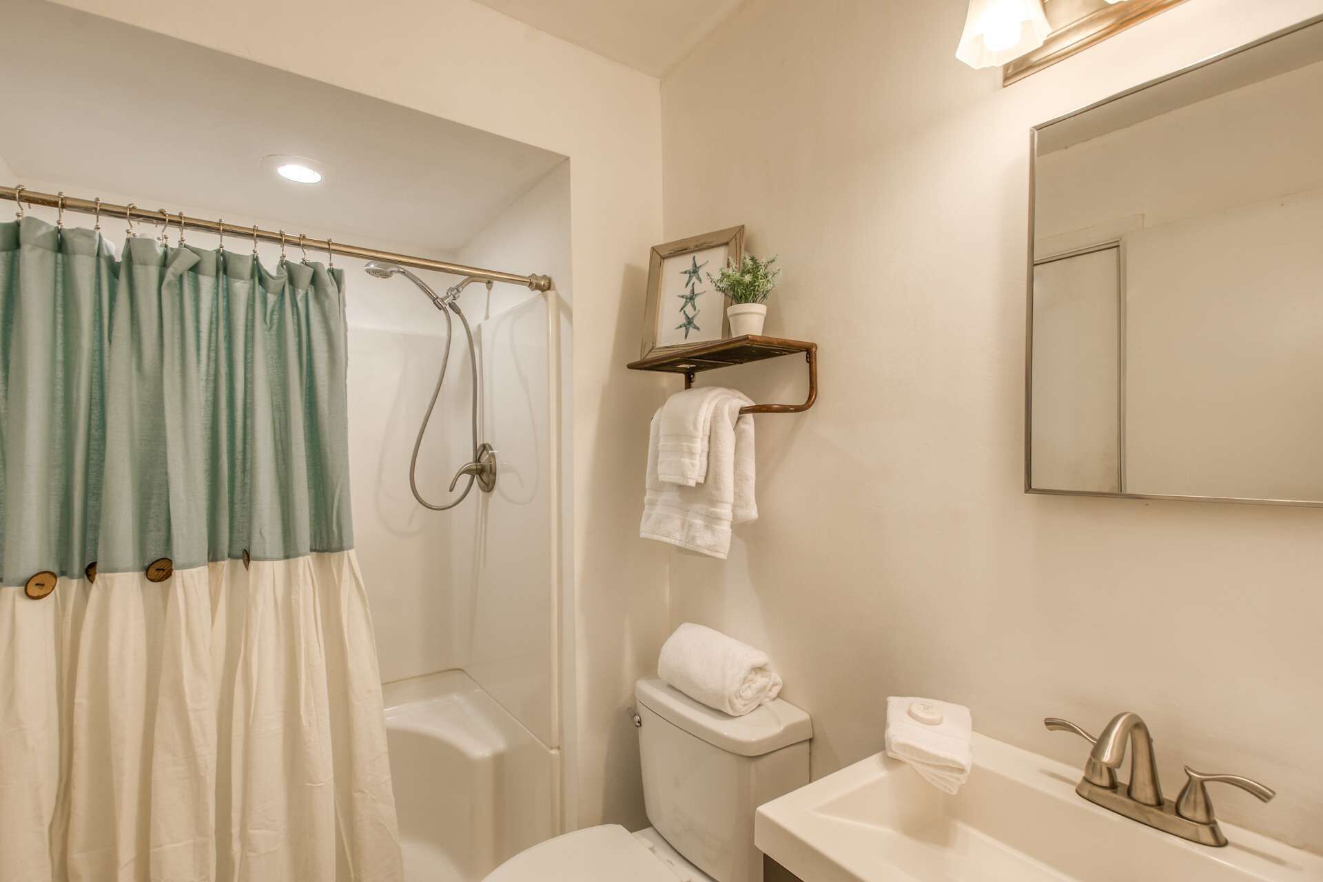 A bathroom with a shower, toilet, sink, and a mirror.