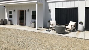 Een wit gebouw met een overdekte patio, twee zwarte deuren en terrasmeubilair met een ronde tafel en stoelen.