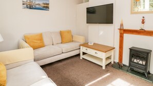 Ein Wohnzimmer mit einem beigen Sofa, einem kleinen Holztisch, einem an der Wand montierten Fernseher, einem Kamin und einem Landschaftsbild.