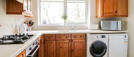 Une cuisine avec des meubles de rangement en bois, une cuisinière, un four à micro-ondes et un lave-linge.