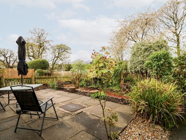 A patio area with a table and chairs, surrounded by a garden with various plants and a wooden fence.