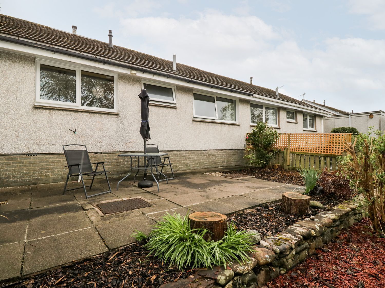 A residential house with a patio area, outdoor seating, and a garden with plants and a wooden fence.