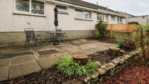 Ein Wohnhaus mit einer Terrasse, Sitzgelegenheiten im Freien und einem Garten mit Pflanzen und einem Holzzaun.
