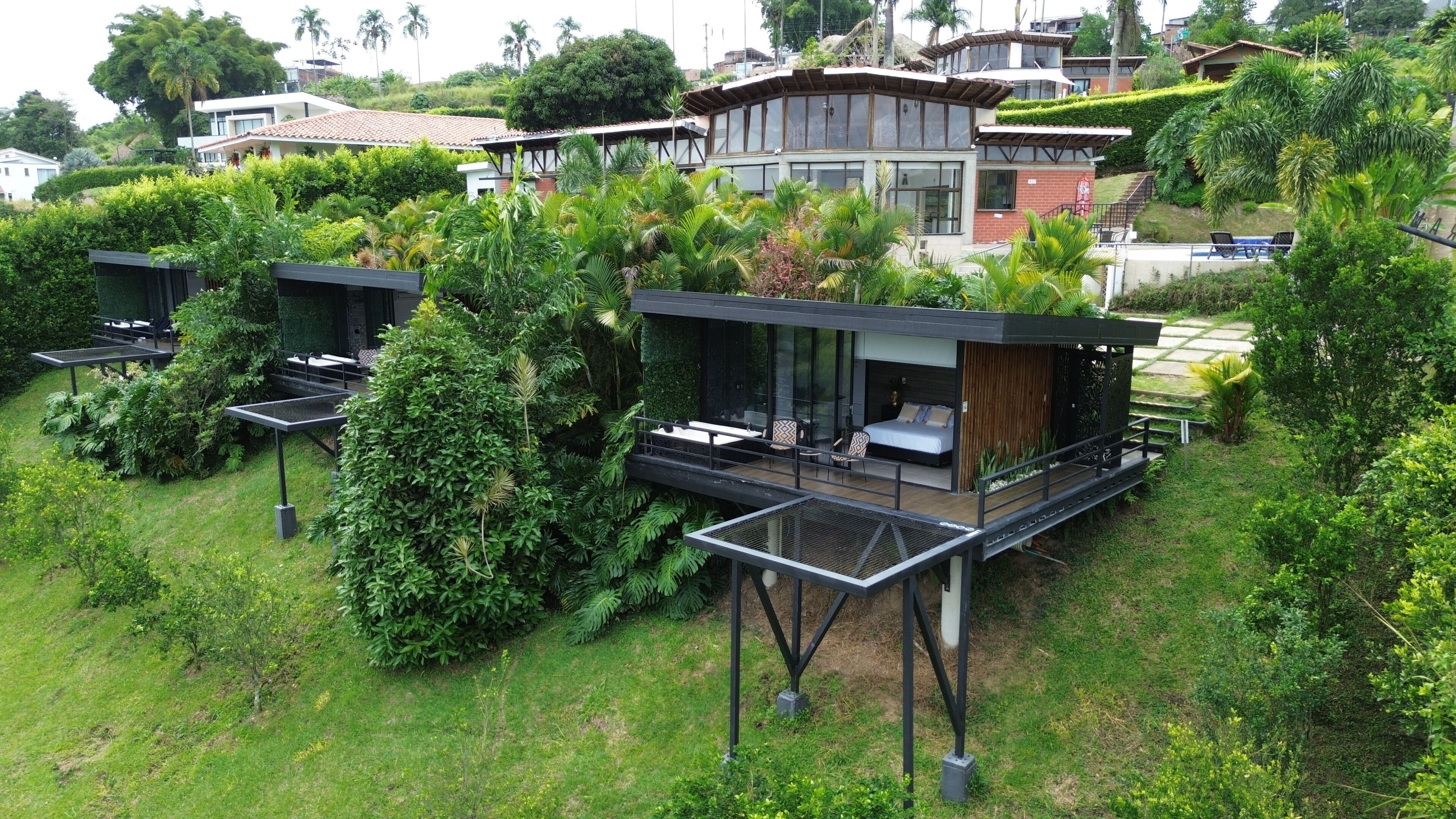 Una villa moderna con un dormitorio envuelto en cristal, zona de estar al aire libre y abundante vegetación.