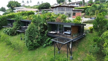 Una villa moderna con un dormitorio envuelto en cristal, zona de estar al aire libre y abundante vegetación.
