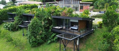 Una villa moderna con un dormitorio envuelto en cristal, zona de estar al aire libre y abundante vegetación.