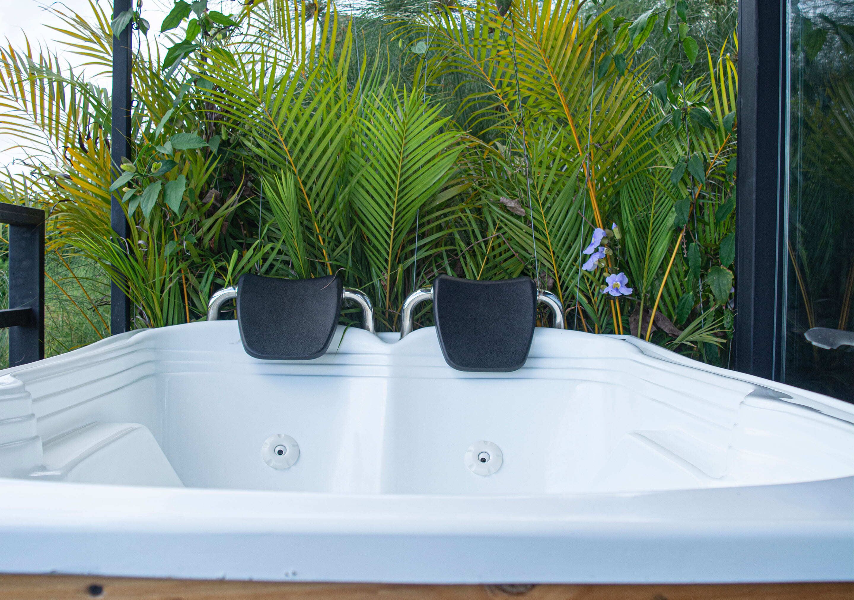 A hot tub with two black seats, surrounded by lush greenery and plants.