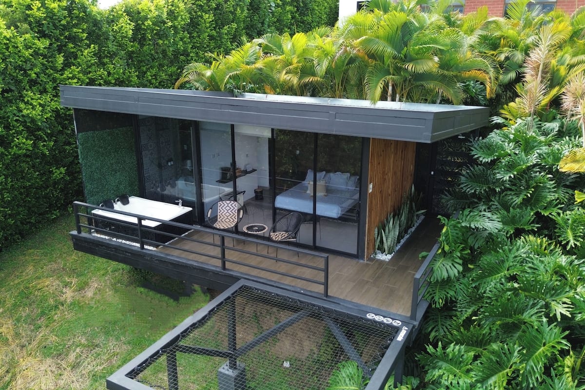 Ein zeitgemäßes Schlafzimmer mit Glasfassade und Balkon, umgeben von üppigem Grün.