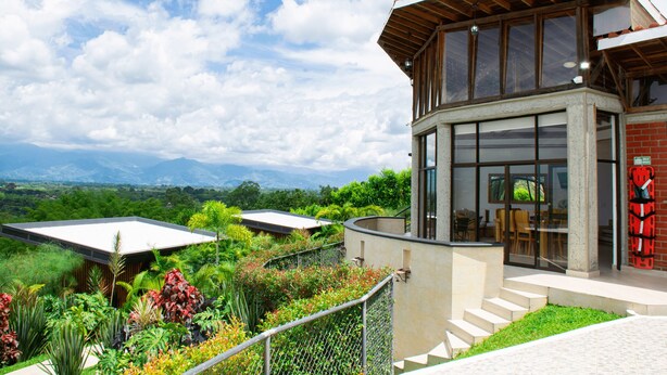 A modern building with large windows, a covered patio, and a view of lush greenery and mountains. - Panorama Pueblo Tapao  (Montenegro)