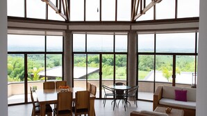 A spacious room with a large table and chairs, a sofa, and a view of a lush landscape through large windows. - Panorama Pueblo Tapao  (Montenegro)