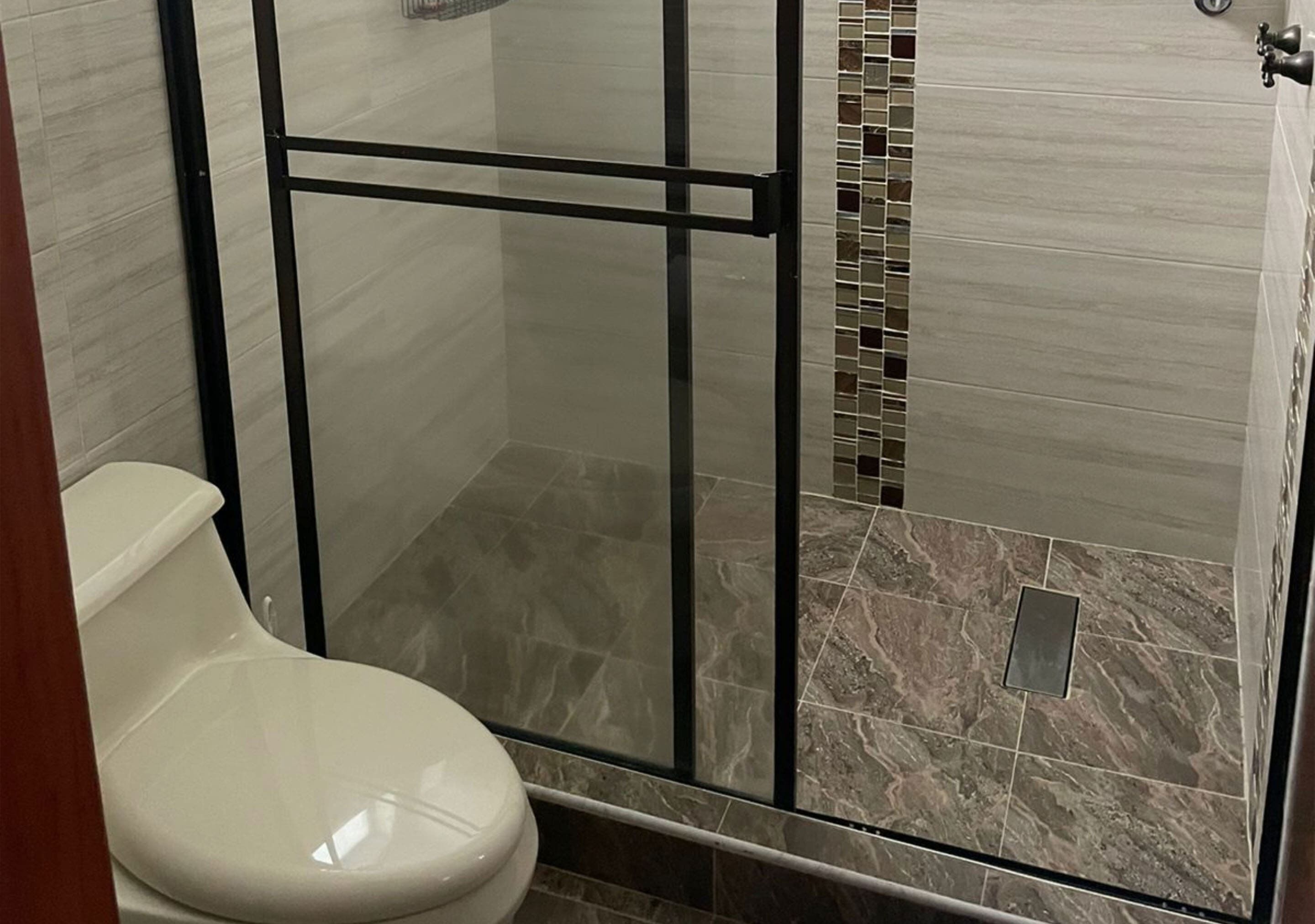 Une salle de bain avec une douche à parois de verre, des toilettes blanches et un sol carrelé.