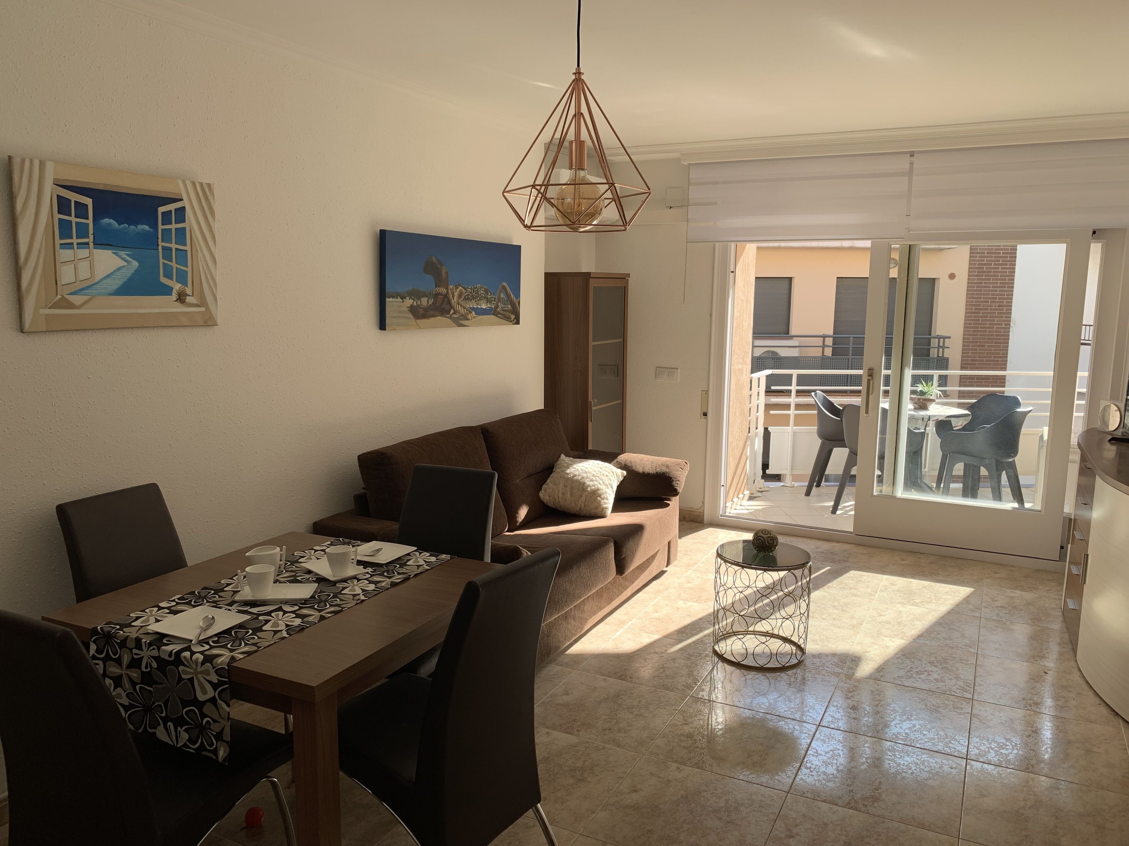 A modern living room with a dining area, a sofa, a coffee table, and a painting of a beach scene.