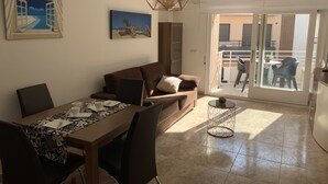 Un salon moderne comprenant un coin repas, un canapé, une table basse et un tableau représentant une scène de plage.