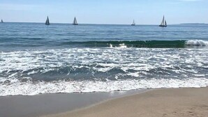 Une plage avec des vagues et des voiliers à l’horizon.