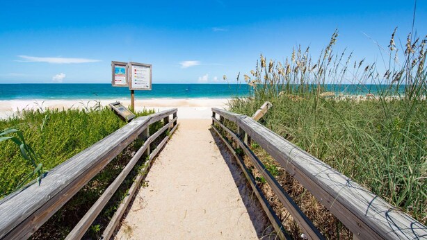 A wooden pathway leading to a beach with a signboard.