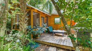 A wooden cabin with a deck, surrounded by lush greenery.