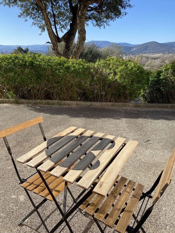 A wooden bench with a metal frame, set on a gravel surface with a tree and bushes in the background. - f1 font mourier cogolin (Cogolin)